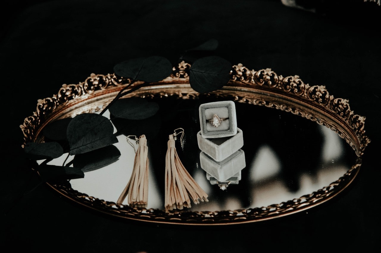 a mirror tray holding an engagement ring in a ring box and a pair of earrings
